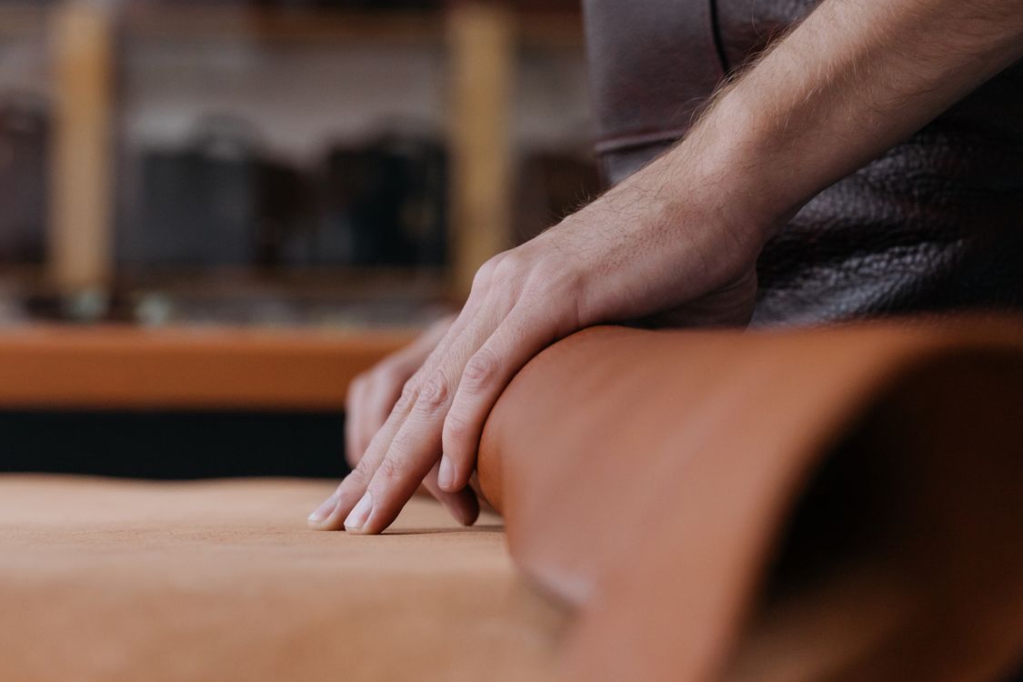 Main posée sur une pièce de cuir cognac roulée dans un atelier