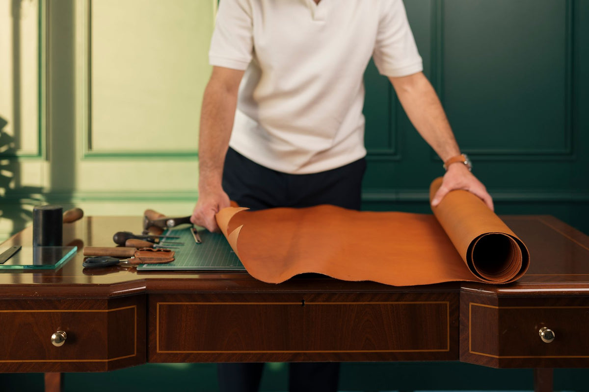 Travail de pièces de cuir et outils sur un établi de maroquinerie.